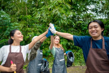 Endonezyalı önlük ve eldiven giyen güneydoğu Asyalılar temizlik faaliyetinden sonra birbirlerine beşlik çakıyorlar. Çöpleri temizleyerek çevreyi korumak.