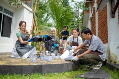Temizlik sırasında önlük ve eldiven giyen Güneydoğu Asyalılar. Çöplerle dolu bir süpürge ve çöp torbası tutuyorum. Çöpleri temizleyerek çevreyi korumak.
