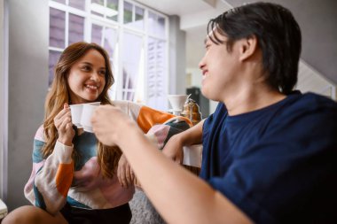Endonezyalı güneydoğu Asyalı çift modern mutfak tezgahlarında kahve içerken neşeli bir anı paylaşıyorlar. Gülümsüyorlar ve birbirlerine bakıyorlar.