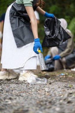 Temizlik sırasında önlük ve eldiven giyen gönüllüler. Çöplerle dolu çöp torbalarını tutarak. Çöpleri temizleyerek çevreyi korumak.