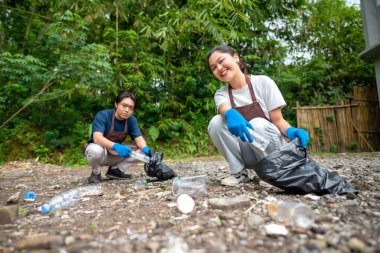 Temizlik sırasında önlük ve eldiven giyen Güneydoğu Asyalılar. Çöplerle dolu çöp torbalarını tutarak. Çöpleri temizleyerek çevreyi korumak.