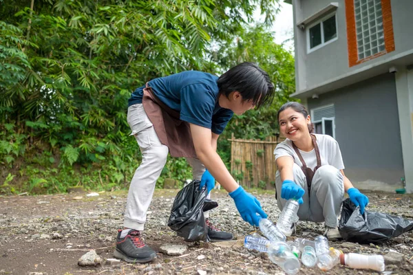 Temizlik sırasında önlük ve eldiven giyen Güneydoğu Asyalılar. Çöplerle dolu çöp torbalarını tutarak. Çöpleri temizleyerek çevreyi korumak.