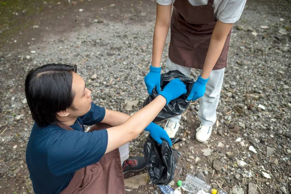 Temizlik sırasında önlük ve eldiven giyen Güneydoğu Asyalılar. Çöplerle dolu çöp torbalarını tutarak. Çöpleri temizleyerek çevreyi korumak.