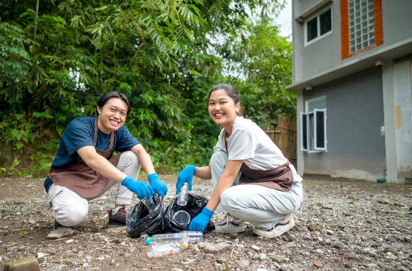 Temizlik sırasında önlük ve eldiven giyen Güneydoğu Asyalılar. Çöplerle dolu çöp torbalarını tutarak. Çöpleri temizleyerek çevreyi korumak.