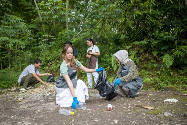 Temizlik sırasında önlük ve eldiven giyen Güneydoğu Asyalılar. Çöplerle dolu çöp torbalarını tutarak. Çöpleri temizleyerek çevreyi korumak.