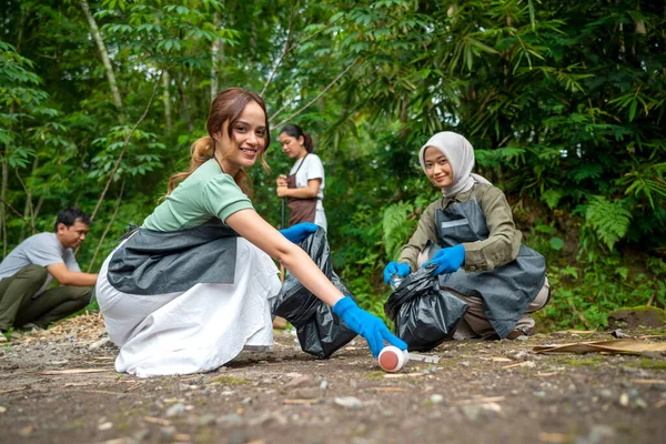 Temizlik sırasında önlük ve eldiven giyen Güneydoğu Asyalılar. Çöplerle dolu çöp torbalarını tutarak. Çöpleri temizleyerek çevreyi korumak.