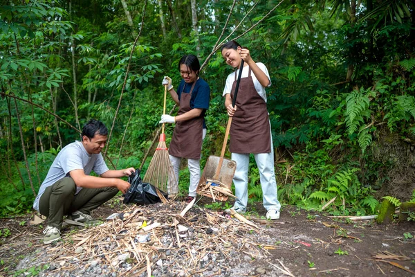 Temizlik sırasında önlük ve eldiven giyen güneydoğu Asyalı erkekler. Çöplerle dolu çöp torbalarını tutarak. Çöpleri temizleyerek çevreyi korumak.