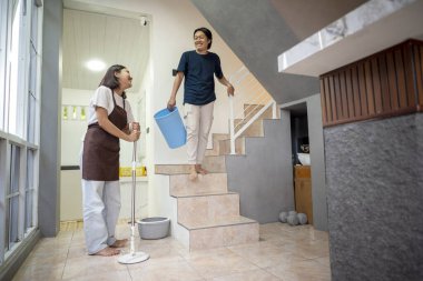 Endonezyalı güneydoğu Asyalı çift, paspas kullanan bir kadın ve kova taşıyan bir adam, evlerinin içini gülümseme ve sıradan pozlarla temizliyor.