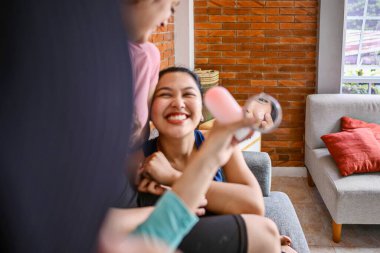 Endonezyalı Güneydoğu Asyalı kadınlar yüz kremi sürüyorlar, gülümsüyorlar ve ciltlerine bakıyorlar.