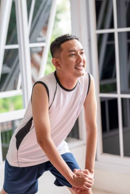 Aktif giyimli Endonezyalı güneydoğu Asyalı bacağını içeride esnetiyor. Sabah rutin egzersizleri, sağlıklı bir yaşam tarzının göstergesi.