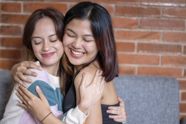 Endonezyalı güneydoğu Asyalı kadınlar modern bir iç mekanda rahat gri bir kanepede dinleniyorlar. Gülüyorlar ve gülümsüyorlar, birlikte hoş ve parlak bir oturma odasında vakit geçiriyorlar.