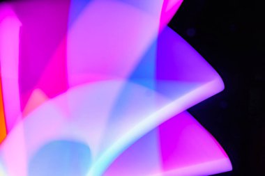 Bulanık efektli ışık resminin soyut görüntüsü. Karanlık arka planda renkli parlak ışıklar kıvrılıyor. Duvar kağıdı, arkaplan veya tasarım ögesi olarak kullanılabilir