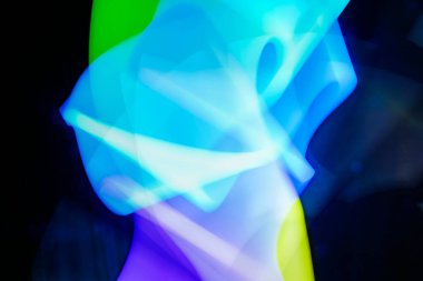 Mavi, yeşil ve mor tonlarında koyu arkaplan üzerinde dinamik ve canlı renkler barındıran soyut ışık resmi. Bulanık, dalgalı ışık çizgileri arasında hareket