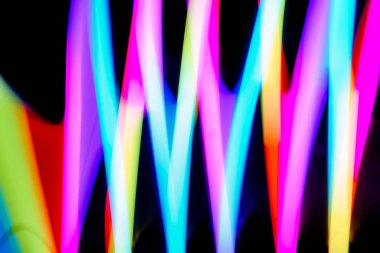 Bulanık efektli ışık resminin soyut görüntüsü. Karanlık arka planda renkli parlak ışıklar kıvrılıyor. Duvar kağıdı, arkaplan veya tasarım ögesi olarak kullanılabilir