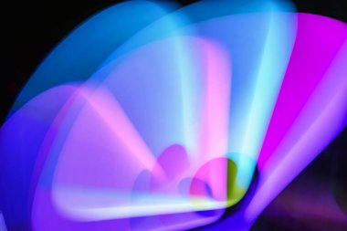 Bulanık efektli ışık resminin soyut görüntüsü. Karanlık arka planda renkli parlak ışıklar kıvrılıyor. Duvar kağıdı, arkaplan veya tasarım ögesi olarak kullanılabilir