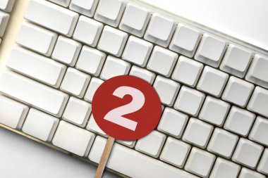 Beyaz bilgisayar klavyesinin yakın plan görüntüsü, üzerinde kırmızı daire işareti olan, basamakları, sıralamaları veya bildirimleri temsil eden, iki numarayı gösteren