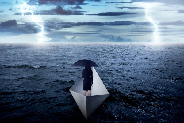 Деловая женщина, держащая зонтик в одиночестве на море, плывущая с бумажной лодкой — стоковое фото