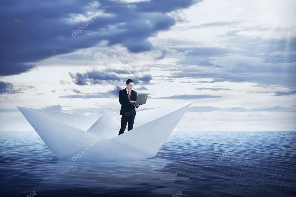 business man working with laptop on the paper boat