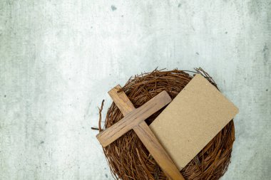 Tahta bir Hıristiyan haçı ve boş bir el işi kağıt kartı. Dini temalar, Paskalya selamları veya sempati kartları için uygun gri desenli bir yüzey üzerinde bir dal yuvada.