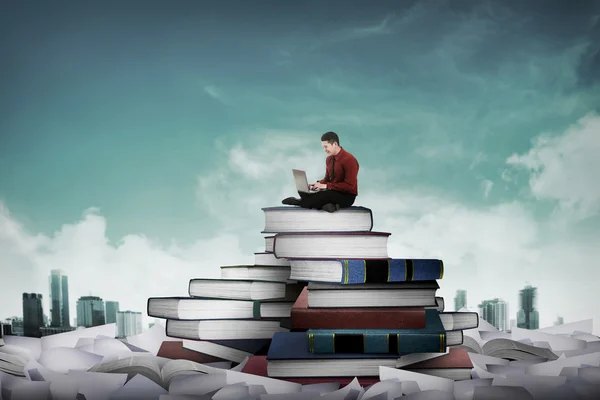 Бизнесмен, работающий с ноутбуком, сидит на вершине книги — стоковое фото