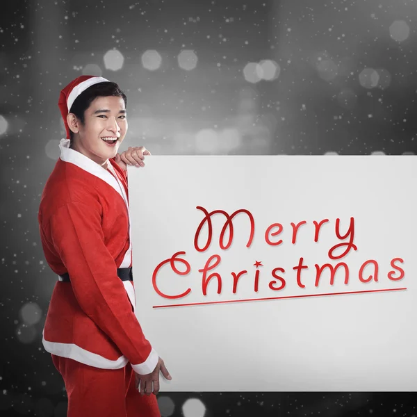 Mann im Weihnachtsmann-Kostüm hält Banner mit fröhlichen Weihnachtsliedern in der Hand — Stockfoto