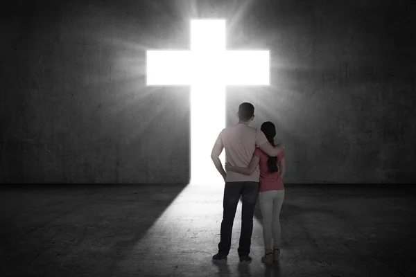 Paar blickt auf das leuchtende Kreuz an der Wand — Stockfoto
