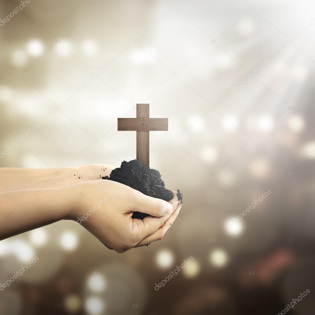 hands holding christian cross with soil