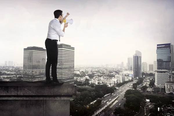 Uomo d'affari utilizzando megafono parlando con la città — Foto Stock