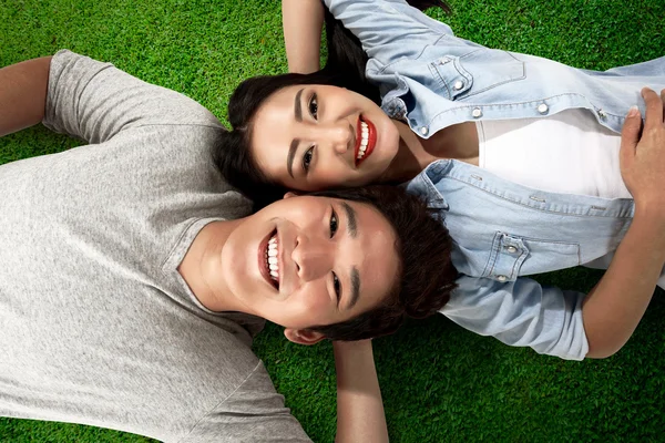 Asian couple lying on green grass — Stock Photo, Image