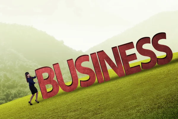 Businesswoman pushing business word uphill — Stock Photo, Image