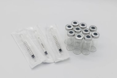 Beyaz bir arka planda plastik paketlerinde on tane tıbbi aşı ampülü ve üç şırınga var. Şırıngalar da aynı şekilde kapalı ve açılmamış..