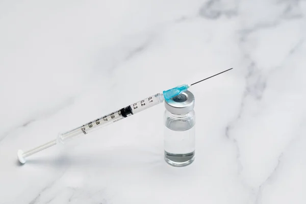 Hypodermic syringe and uncapped needle resting on a vaccine ready vial