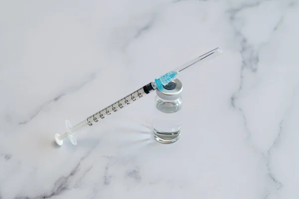 Medical syringe and needle for hypodermic injection on a marble counter top. The syringe and needle are capped.