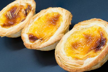 Koyu gri arka planda üç küçük kremalı tart..