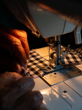 Yaşlı kadın elleri elektrikli dikiş makinesiyle kumaş dikiyor. Kıdemli İşçi ve El Sanatları.