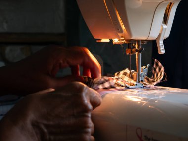 Dikiş makinesiyle çalışan kıdemli kadın. Yaşlı Eller Yetenekli İş gücü vasıtasıyla Giysi Oluşturuyor