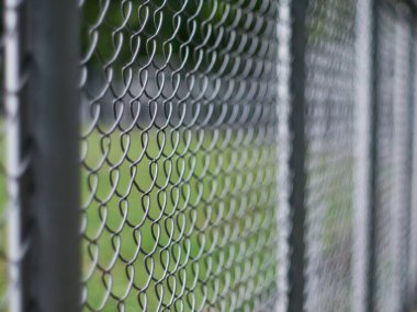 Close-Up of Chain Link Fence with Shallow Depth of Field - Metal Wire Mesh Barrier with Blurred Green Background
