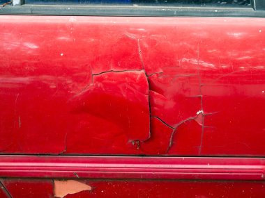 Çarpışmadan dolayı kapı kolunda derin çizikler ve çatlak boyayla ağır hasar görmüş kırmızı bir araba kapısı var.