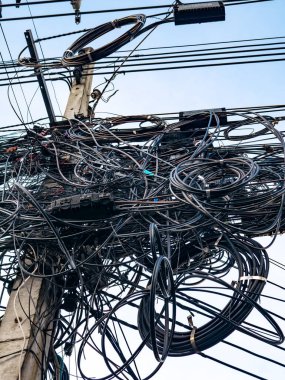 Karmaşık elektrik kabloları ve elektrik kabloları mavi gökyüzüne karşı elektrik direğinde kaotik altyapı gösteriyor.