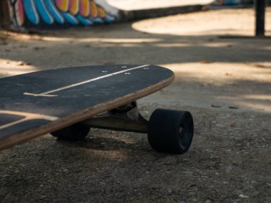 Arka planda graffiti rampası olan terk edilmiş kaykay parkında beton zeminde yatan eski yıpranmış sörf kaykayı.