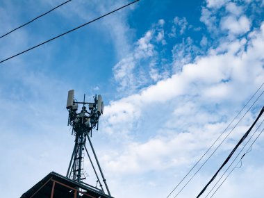 Hücresel telekomünikasyon kulesi anten ve ekipmanlarla beyaz bulutlu mavi gökyüzüne ve elektrik hatlarına karşı