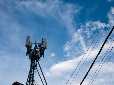 Hücresel telekomünikasyon kulesi anten ve ekipmanlarla beyaz bulutlu mavi gökyüzüne ve elektrik hatlarına karşı