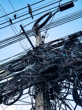 Karmaşık elektrik kabloları ve elektrik kabloları mavi gökyüzüne karşı elektrik direğinde kaotik altyapı gösteriyor.