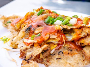 Çıtır Tayland İstiridye Omleti (Hoi Tod) üzerine tatlı acı biber sosu ve taze taze taze soğan konmuş beyaz tabakta