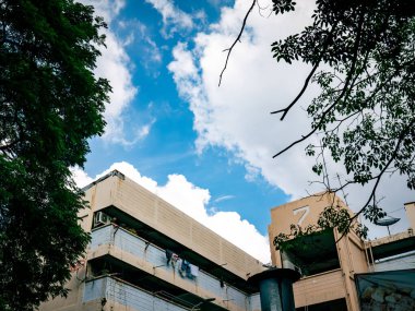 Beyaz bulutlu, kentsel konutlu ve mimarisi olan parlak mavi gökyüzünün altındaki eski beton binanın alçak açılı görüntüsü.