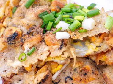 Çıtır Tayland İstiridye Omleti (Hoi Tod) taze fasulye filizi ve beyaz tabakta taze soğanla servis edilir.