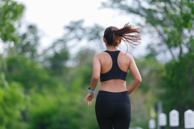 Siyah spor giysili kadın koşucu yeşil ormanda koşuyor..