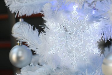 Beyaz Noel ağacında asılı bir kar tanesi oyuncağı biraz ışıkla parıldıyor ve parlıyor.