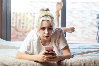 Çekici, sevimli, sevimli, sevimli, çekici, çekici, neşeli, sarışın bir kadının yakın plan portresi. Yatakta uzanmış, erkek arkadaşıyla veya kocasıyla sohbet ediyor. Açık beyaz iç mekanda.