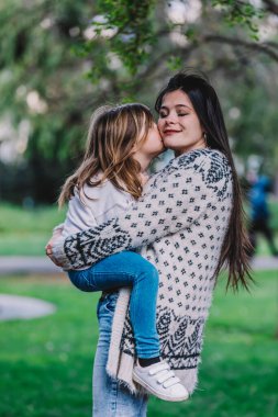 Küçük tatlı kız bebek yanaktan öpüyor ve sarılıyor, yeşil parkta mutlu güzel bir kadınla kucaklaşıyor..